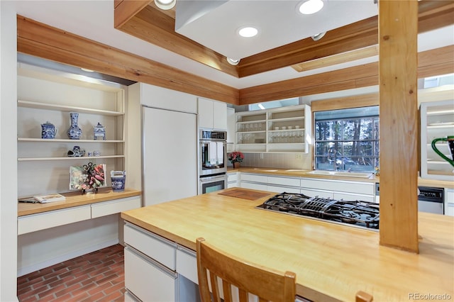 kitchen featuring sink, appliances with stainless steel finishes, a tray ceiling, built in desk, and white cabinets