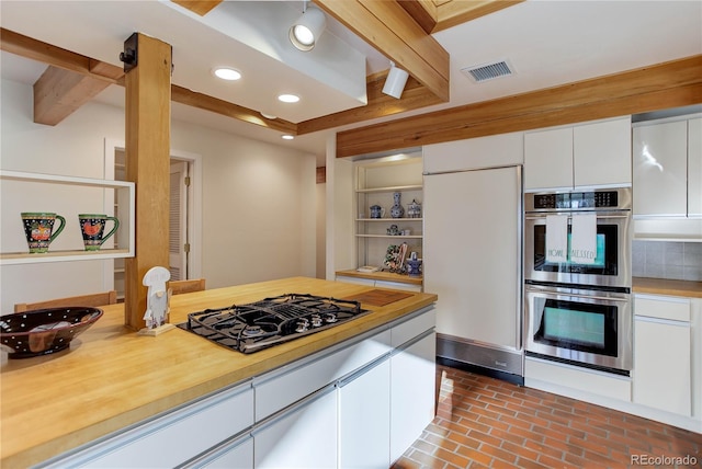 kitchen featuring beam ceiling, white cabinetry, paneled built in fridge, double oven, and black gas cooktop