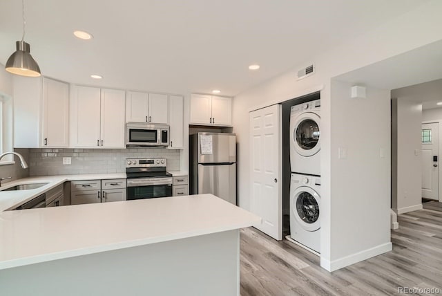 kitchen featuring kitchen peninsula, stainless steel appliances, decorative light fixtures, stacked washer / dryer, and white cabinets