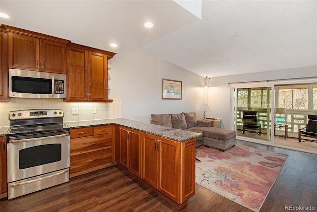 kitchen featuring dark wood-type flooring, stainless steel appliances, decorative backsplash, vaulted ceiling, and kitchen peninsula