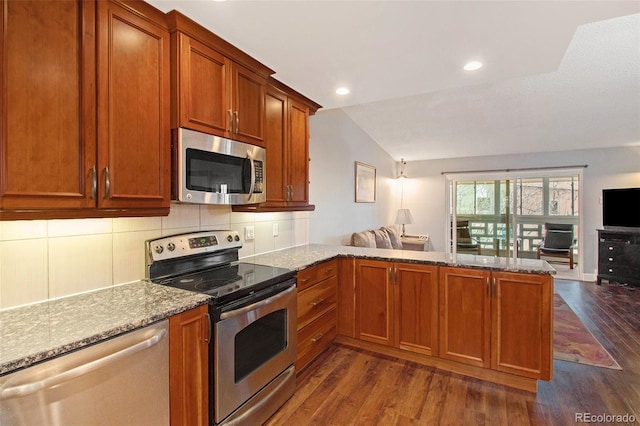 kitchen with dark hardwood / wood-style flooring, light stone counters, stainless steel appliances, and kitchen peninsula