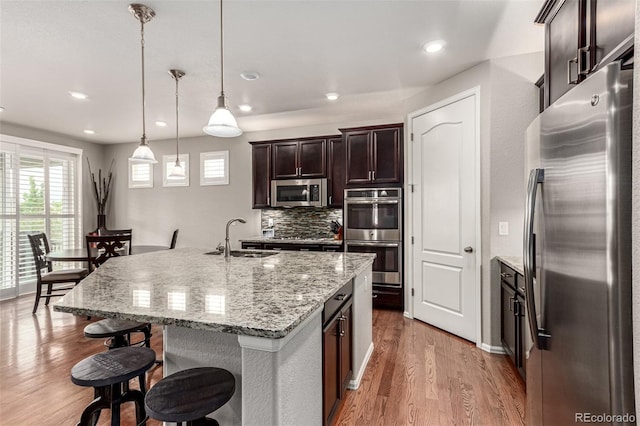7991 Heritage Dr, Thornton, CO 80602 - kitchen featuring appliances with stainless steel finishes, a sink, wood finished floors, a breakfast bar, and tasteful backsplash
