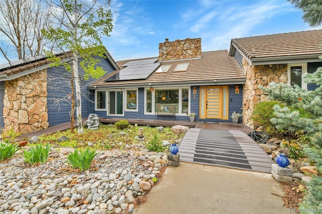 view of front of property with a chimney, roof mounted solar panels, and stone siding