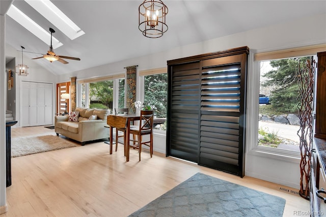 living room with visible vents, light wood-style floors, lofted ceiling with skylight, and ceiling fan with notable chandelier