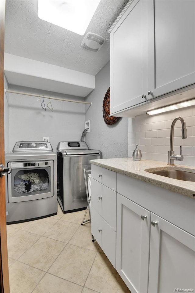 washroom featuring a textured ceiling, a sink, cabinet space, independent washer and dryer, and light tile patterned floors