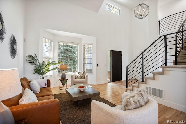 living room with a notable chandelier, visible vents, stairway, a towering ceiling, and light wood-style floors