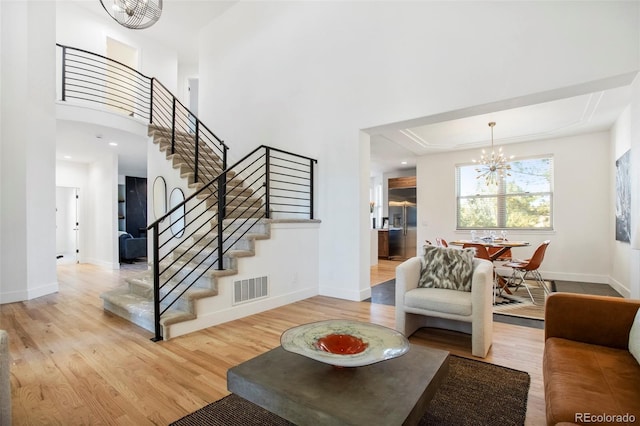 living area featuring visible vents, baseboards, light wood-style flooring, stairway, and an inviting chandelier