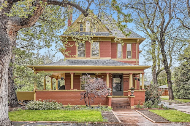 victorian house with covered porch, roof with shingles, and brick siding