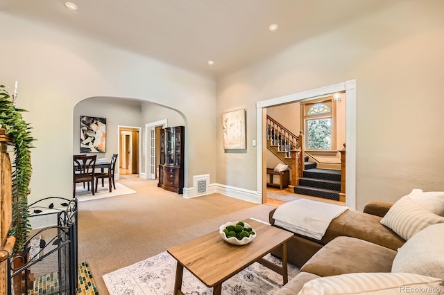 living room featuring arched walkways, light colored carpet, baseboards, stairs, and recessed lighting