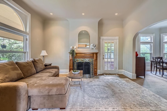 living room featuring arched walkways, recessed lighting, a tiled fireplace, and baseboards