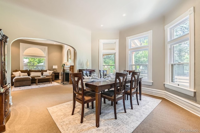 dining room featuring arched walkways, light carpet, a fireplace, and recessed lighting