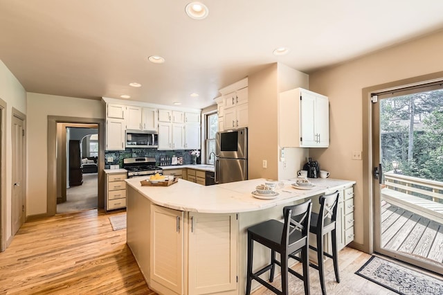 kitchen with stainless steel appliances, a peninsula, light wood-style floors, light countertops, and backsplash