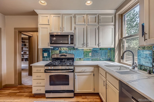 kitchen featuring appliances with stainless steel finishes, a sink, tasteful backsplash, recessed lighting, and light stone counters