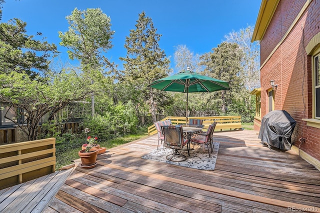 deck with outdoor dining area, area for grilling, a fenced backyard, and view of wooded area