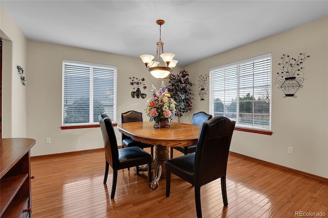 dining area with baseboards, light wood-type flooring, and an inviting chandelier