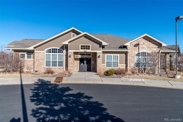 craftsman house with driveway, stone siding, and a shingled roof