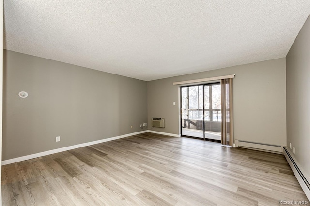 empty room featuring baseboard heating, a textured ceiling, a wall unit AC, and light wood-type flooring