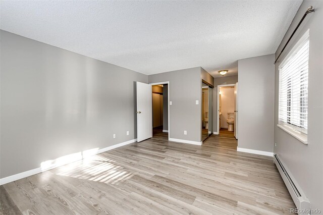 unfurnished bedroom featuring light wood-type flooring, a textured ceiling, a baseboard heating unit, and ensuite bathroom