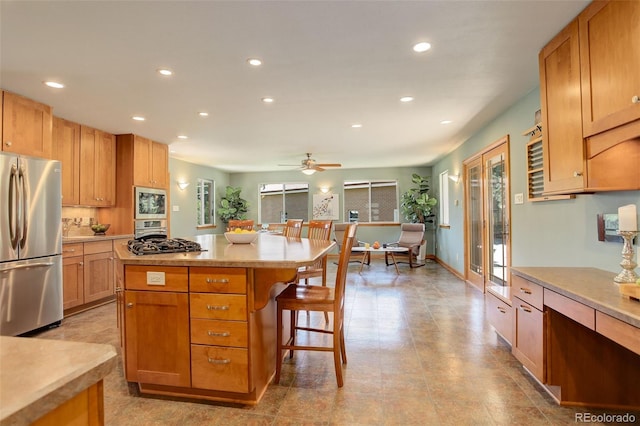 kitchen with ceiling fan, appliances with stainless steel finishes, a kitchen breakfast bar, and a center island