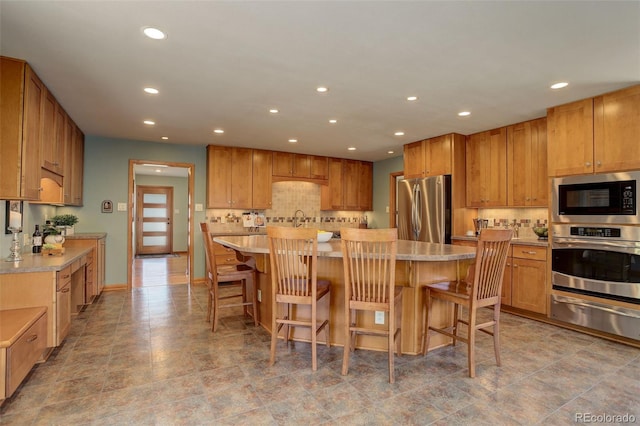 kitchen with tasteful backsplash, appliances with stainless steel finishes, a center island, and a kitchen bar