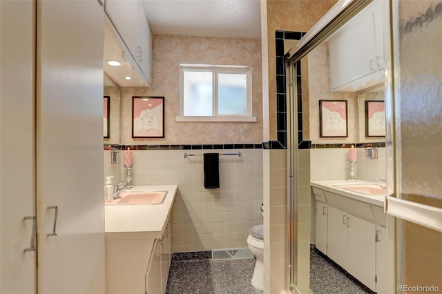 bathroom with tile walls, vanity, a shower with door, and toilet