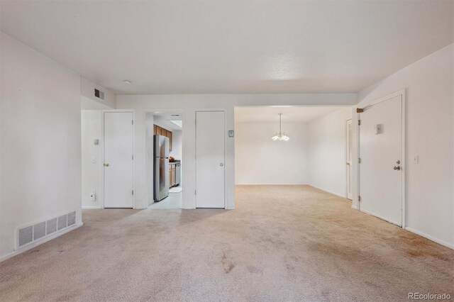 empty room with carpet flooring, a chandelier, and baseboards