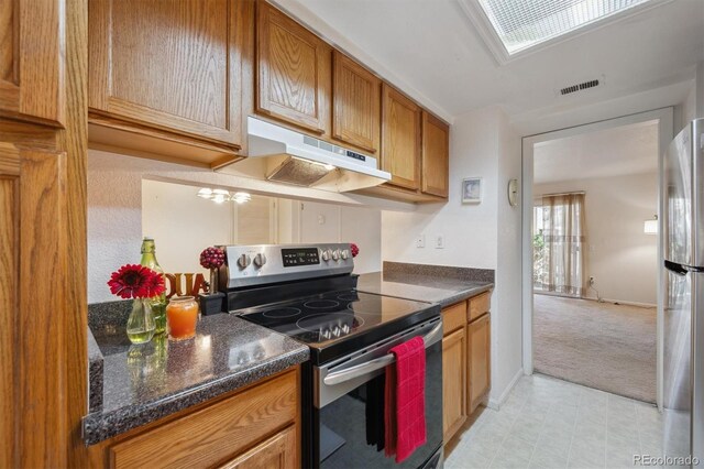 kitchen with appliances with stainless steel finishes, under cabinet range hood, dark countertops, brown cabinets, and light carpet