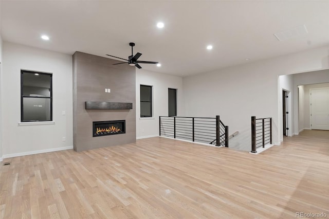 unfurnished living room featuring ceiling fan, a large fireplace, and light wood-type flooring