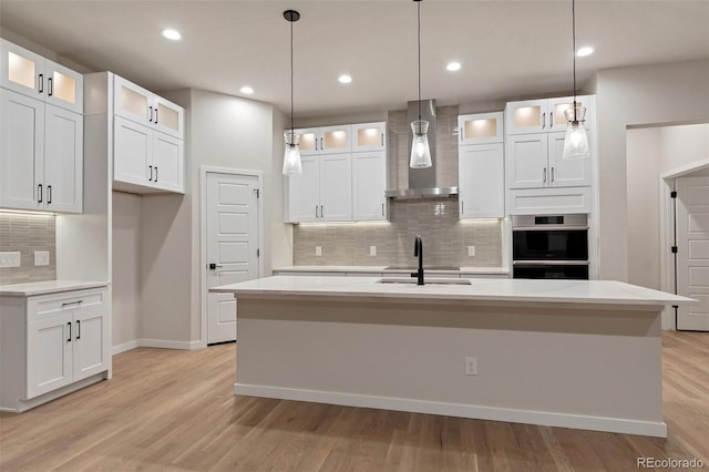 kitchen with white cabinetry, a center island with sink, and wall chimney exhaust hood