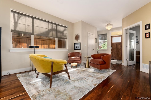 living area with baseboards, a notable chandelier, visible vents, and wood finished floors
