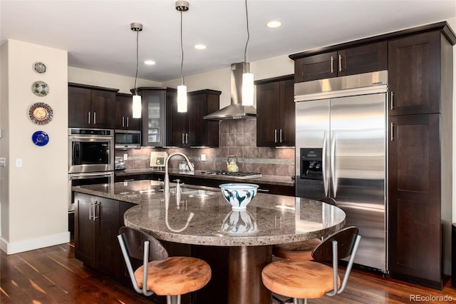 kitchen with stainless steel appliances, wall chimney exhaust hood, a sink, and dark wood-style flooring