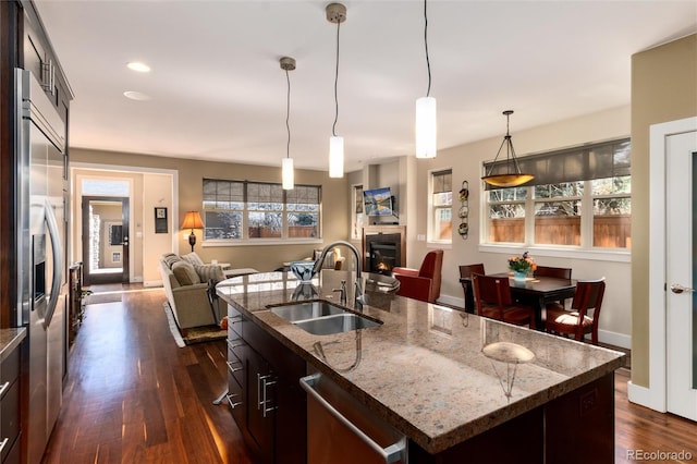 kitchen featuring a sink, stainless steel appliances, a warm lit fireplace, open floor plan, and dark wood finished floors