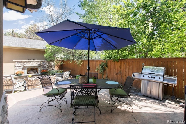 view of patio with an outdoor stone fireplace, area for grilling, fence, and outdoor dining space