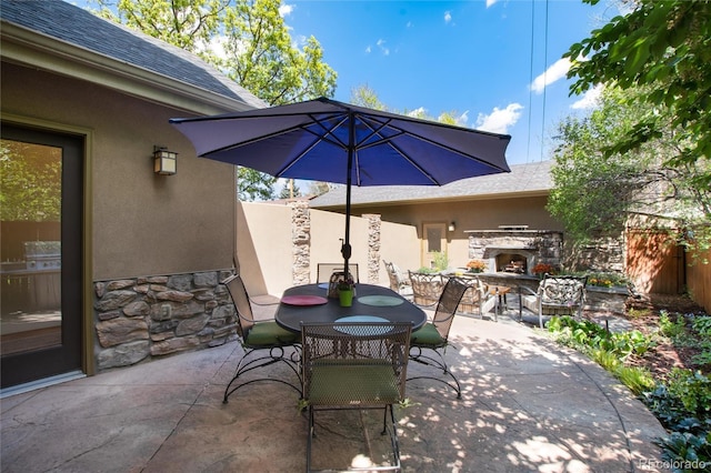 view of patio with an outdoor stone fireplace, outdoor dining space, and fence