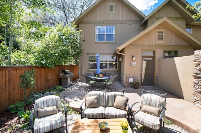 back of house with a patio area, fence, board and batten siding, stucco siding, and stone siding