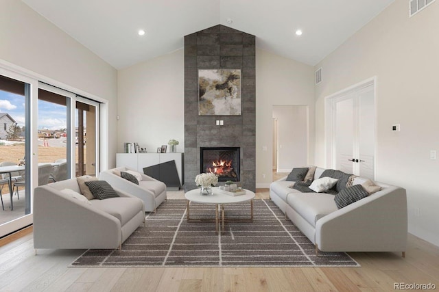 living room featuring a tile fireplace, high vaulted ceiling, and light hardwood / wood-style flooring