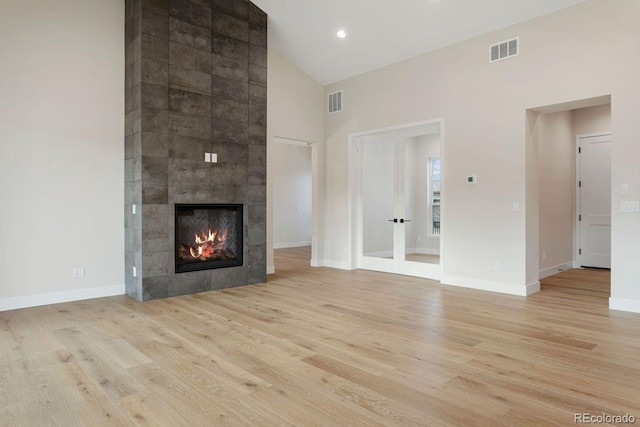 unfurnished living room with light hardwood / wood-style floors, high vaulted ceiling, and a tiled fireplace