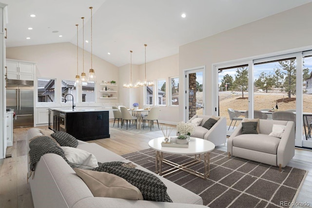 living room featuring sink, high vaulted ceiling, a notable chandelier, and light wood-type flooring