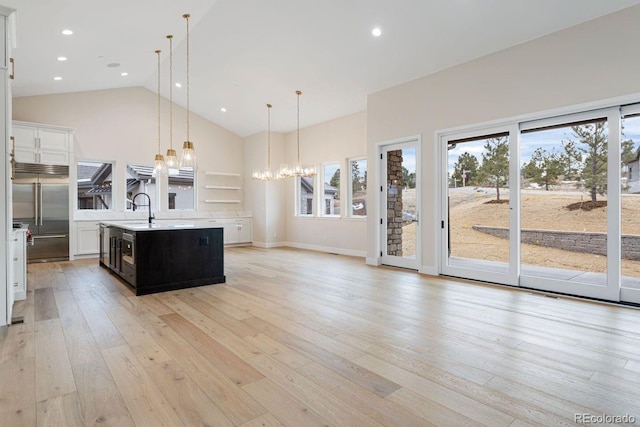 kitchen featuring a kitchen island with sink, light hardwood / wood-style flooring, stainless steel built in fridge, a chandelier, and hanging light fixtures