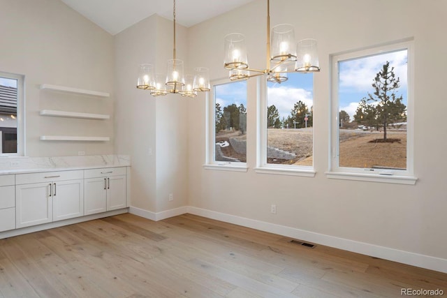 unfurnished dining area with a chandelier, light hardwood / wood-style flooring, and lofted ceiling