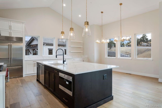 kitchen with a kitchen island with sink, hanging light fixtures, sink, light stone counters, and stainless steel appliances