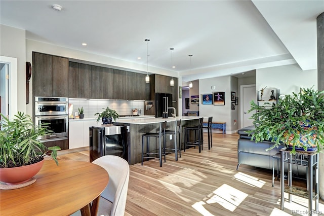 kitchen with pendant lighting, black refrigerator, an island with sink, dark brown cabinets, and light hardwood / wood-style floors