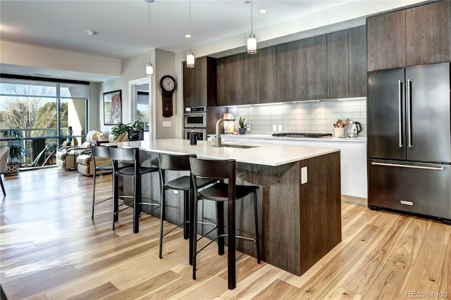 kitchen with backsplash, sink, hanging light fixtures, an island with sink, and stainless steel appliances