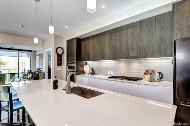 kitchen featuring stainless steel appliances, tasteful backsplash, light countertops, a sink, and modern cabinets