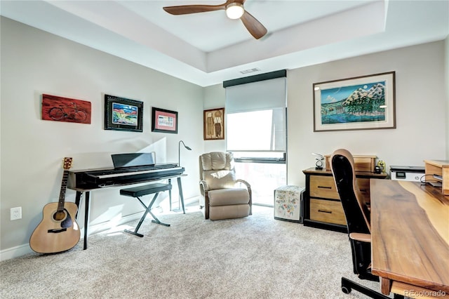 carpeted home office featuring a tray ceiling and ceiling fan