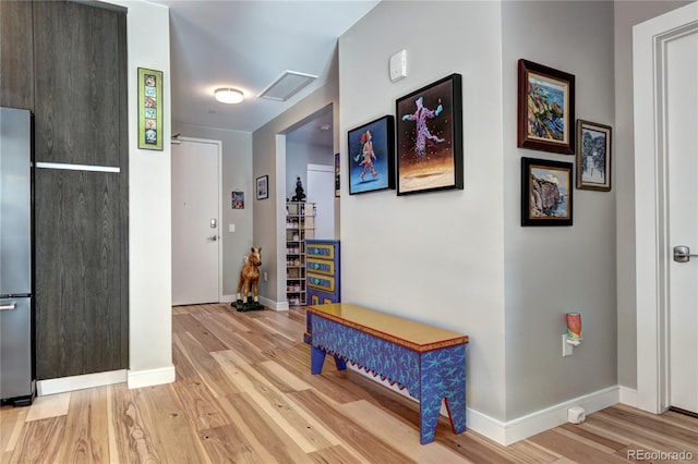 hallway featuring light wood-type flooring, attic access, visible vents, and baseboards