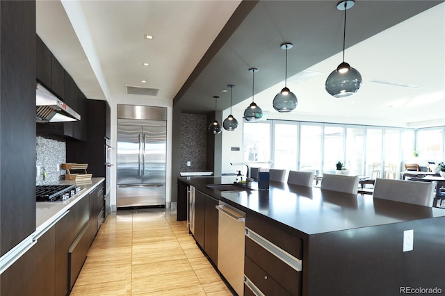 kitchen featuring tasteful backsplash, appliances with stainless steel finishes, a large island with sink, under cabinet range hood, and a sink