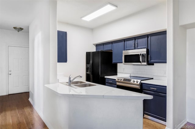 kitchen with blue cabinetry, sink, appliances with stainless steel finishes, kitchen peninsula, and backsplash