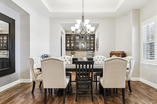 dining space featuring dark wood-type flooring, a raised ceiling, and a chandelier