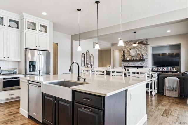 kitchen with pendant lighting, white cabinets, light stone counters, stainless steel appliances, and light wood-type flooring